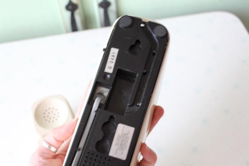 May include: White rotary phone with a black base and a black cord. The phone has a number "G 0491" printed on the back.