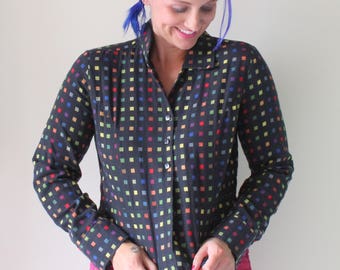 Puede incluir: Una camisa negra de manga larga con botones y un estampado geométrico colorido. La camisa tiene cuello y una silueta ajustada.