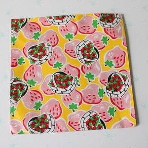 May include: Yellow fabric with a repeating pattern of pink strawberries in baskets. The strawberries are red with green leaves and the baskets are white with black outlines.