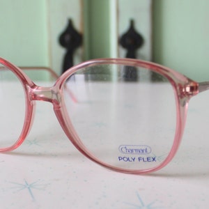 May include: Pink plastic framed eyeglasses with clear lenses. The brand name "Charmart" and "POLY FLEX" are printed on the right lens.