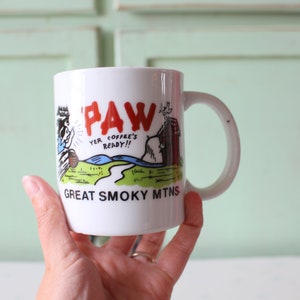 Può includere: Tazza da caffè in ceramica bianca con un'illustrazione di un orso che tiene una caffettiera e il testo "Paw Yer Coffee's Ready!!" e "Great Smoky Mtns."