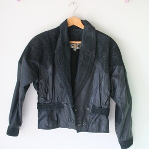 May include: A black leather jacket with a suede collar and trim. The jacket has a double breasted closure and a belt at the waist.