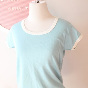 May include: A light blue t-shirt with white trim around the neckline and sleeves.