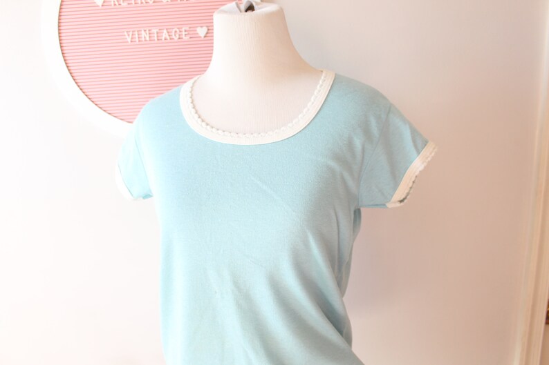 May include: A light blue t-shirt with white trim around the neckline and sleeves.