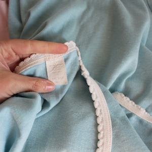 May include: A light blue garment with white lace trim. The garment has a white tag with text that is too blurry to read.