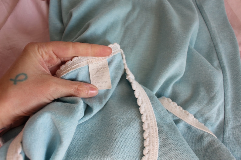 May include: A light blue garment with white lace trim. The garment has a white tag with text that is too blurry to read.