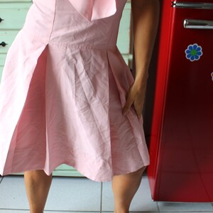 May include: A woman wearing a pink dress stands in front of a red refrigerator with flower decals.