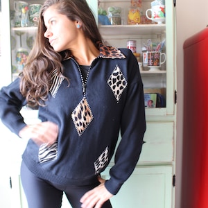 May include: A black sweater with a zipper closure and diamond-shaped patches of animal print fabric. The patches are made of zebra, leopard, and cheetah print fabric.