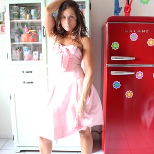 May include: A woman in a pink strapless dress stands in front of a red refrigerator with flower stickers. The refrigerator has the word "GALANZ" on the front.