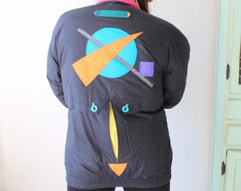 May include: A black puffer jacket with a geometric design on the back. The design features a blue circle, orange and yellow lines, and a purple square.