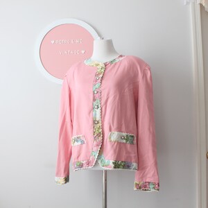 May include: A pink vintage jacket with floral trim and button details. The jacket has a scalloped hem and long sleeves.