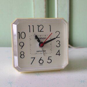 Peut inclure: Un réveil carré blanc avec des chiffres et des aiguilles noirs. Le cadran de l'horloge indique "Graham Lighted Dial USA".