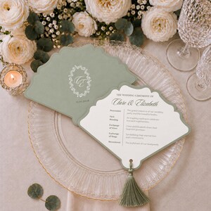 Könnte beinhalten: Ein fächerförmiges Hochzeitskarten-Programm in Salbeigrün mit gewelltem Rand und passender Quaste. Die Vorderseite zeigt ein weißes Blumenmonogramm mit den Initialen CE und dem Datum 12.05.2018. Das Innere listet den Ablauf der Hochzeitszeremonie auf.