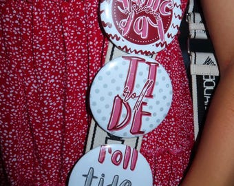 May include: Three round buttons with text and designs in red and white. The top button says "Some Alabama Joy" in a cursive font. The middle button says "Tide" and "DE" in a pink font. The bottom button says "Roll Tide Roll".