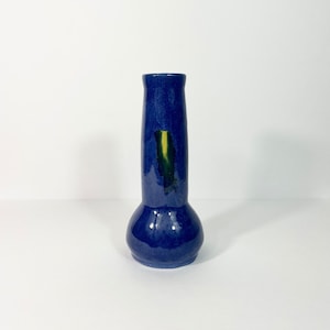 May include: A small, blue ceramic vase with a yellow and green glaze detail. The vase has a rounded bottom and a narrow neck.