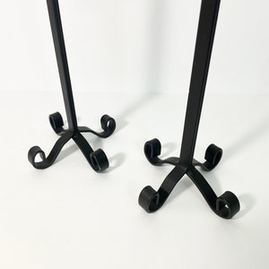 Pode incluir: Dois casti&ccedil;ais de metal preto com um design simples e elegante. Cada casti&ccedil;al tem um caule alto e fino e uma base com quatro p&eacute;s enroladas.