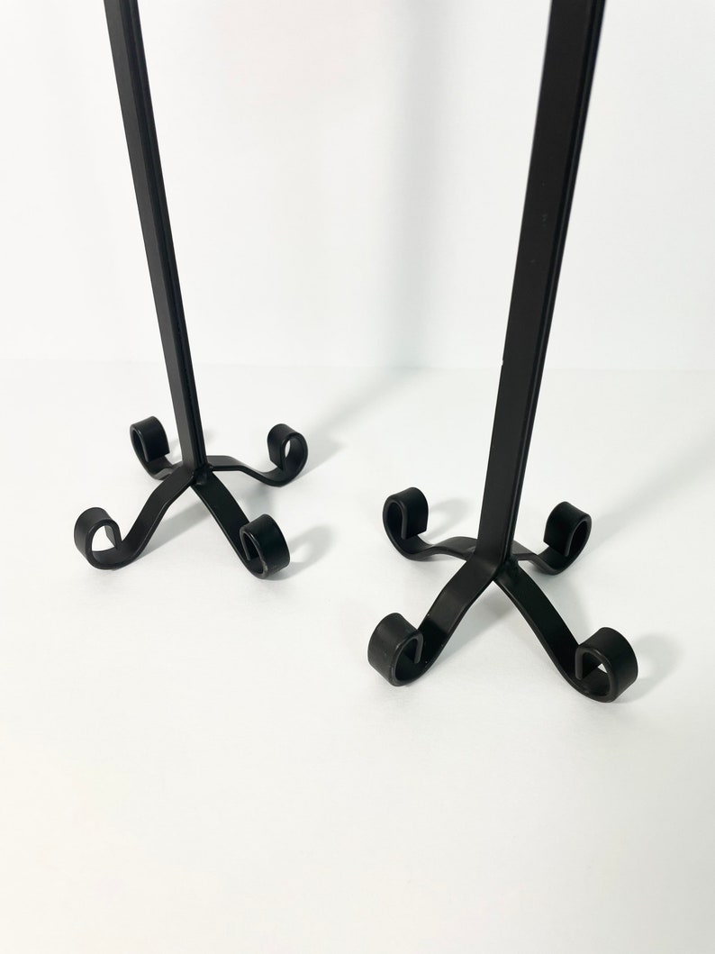 Pode incluir: Dois casti&ccedil;ais de metal preto com um design simples e elegante. Cada casti&ccedil;al tem um caule alto e fino e uma base com quatro p&eacute;s enroladas.