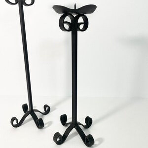 Pode incluir: Dois casti&ccedil;ais de metal preto com um design de rolagem. Os casti&ccedil;ais s&atilde;o altos e finos com uma base redonda.