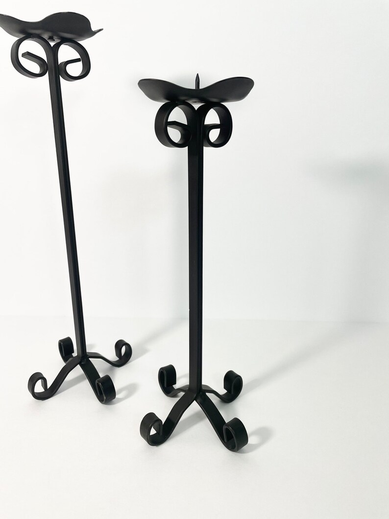 Pode incluir: Dois casti&ccedil;ais de metal preto com um design de rolagem. Os casti&ccedil;ais s&atilde;o altos e finos com uma base redonda.