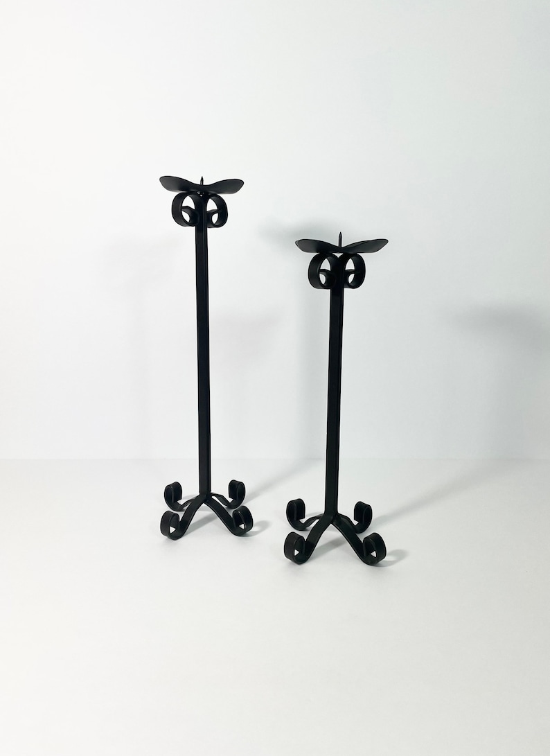 Pode incluir: Um par de casti&ccedil;ais de metal preto com um design de rolagem. Os casti&ccedil;ais s&atilde;o altos e finos, com uma base simples e um topo decorativo.