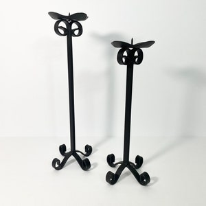 Pode incluir: Um conjunto de dois casti&ccedil;ais de metal preto com um design simples e elegante. Cada casti&ccedil;al possui uma base com volutas e um &uacute;nico porta-velas.