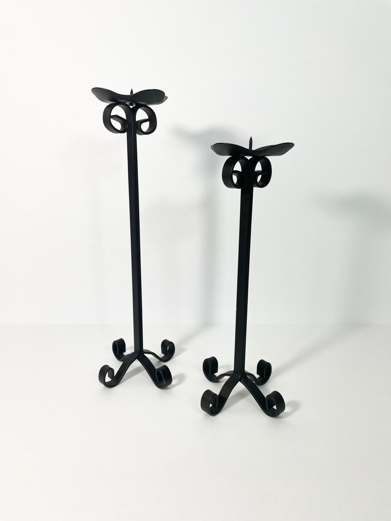Pode incluir: Um conjunto de dois casti&ccedil;ais de metal preto com um design simples e elegante. Cada casti&ccedil;al possui uma base com volutas e um &uacute;nico porta-velas.