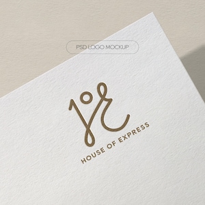 May include: A close-up of a white paper with a gold logo that reads "jr" with a circle above the "j" and the words "HOUSE OF EXPRESS" below the logo. The words "PSD LOGO MOCKUP" are at the top.