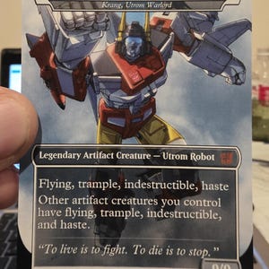 Könnte beinhalten: Sammelkarte mit einem Roboter namens "Superion, Aerialbot Apotheosis." Die Karte hat einen weißen Rand und einen blauen Hintergrund. Der Roboter ist hauptsächlich rot, weiß und gelb. Text enthält "Flying, trample, indestructible, haste."