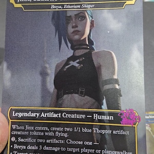 May include: A Magic: The Gathering card featuring "Jinx, Sadistic Tinkerer." The card shows a portrait of a woman with blue hair and a black outfit. Text includes "Legendary Artifact Creature - Human" and game instructions. The card is marked 4/4.