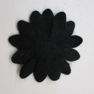 May include: A black felt flower with rounded petals, arranged in a circular pattern. The flower is centered against a white background. The felt has a slightly textured appearance.