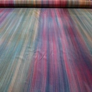 May include: A roll of fabric with a vibrant, multicolored striped pattern. The fabric features vertical stripes in shades of blue, pink, red, and purple. The fabric is rolled up at the top, showing the edge of the material.