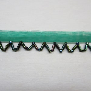 May include: Green mesh trim with a beaded edge. The beads are iridescent and have a dark green, blue, and black color.