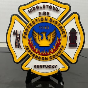 May include: A multi-layered, decorative fire department emblem. The emblem features the words "Middletown Fire Protection District Jefferson County Kentucky" and the year "1940". The emblem is white, yellow, black, red, and blue.