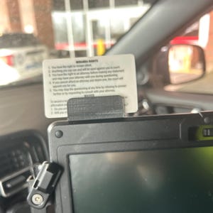 Puede incluir: Una tableta negra con pantalla está montada en un vehículo. Una tarjeta blanca con el texto "Miranda Rights" está sujeta a la parte superior de la tableta. La tarjeta enumera derechos como el derecho a guardar silencio y a un abogado.