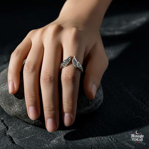 Multiple angle view of gothic angel wing ring in 925 sterling silver showing adjustable band flexibility. Wings maintain detailed feather structure while band adapts to finger size. Dark moody photography emphasizes gothic romance and fallen angel symbolism.