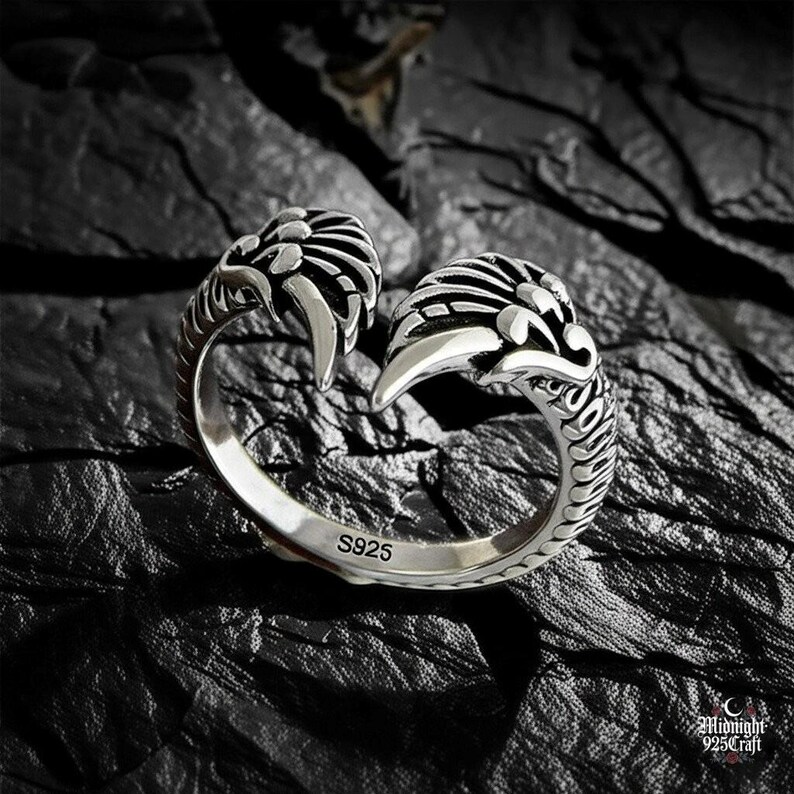 Dramatic lighting on gothic angel wing ring showcasing feather texture and silver reflections. Adjustable 925 sterling silver band with celestial wing motif, photographed against dark slate background. Ideal for witchy aesthetic, dark romantic style, fallen angel theme jewelry.