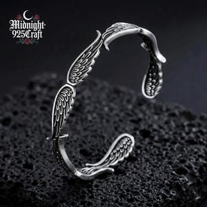 Angled view of the 925 sterling silver angel wing cuff bracelet worn on a wrist, showing how the open bangle wraps comfortably around the skin. The retro oxidized Thai silver finish is evident with feather-engraved wing motifs visible from this angle — a unique handmade gothic bracelet.
