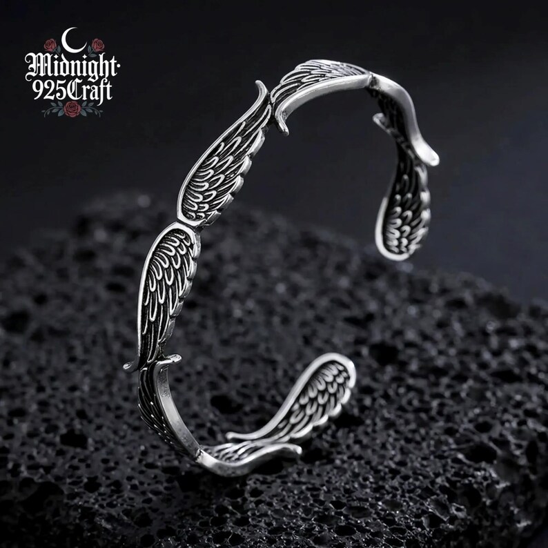 Angled view of the 925 sterling silver angel wing cuff bracelet worn on a wrist, showing how the open bangle wraps comfortably around the skin. The retro oxidized Thai silver finish is evident with feather-engraved wing motifs visible from this angle — a unique handmade gothic bracelet.