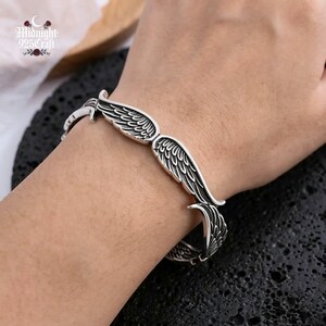 May include: A silver-colored bracelet with a wing design. The bracelet features detailed feather patterns and is worn on a wrist. The brand name "Midnight 925 Craft" is visible in the upper left corner.