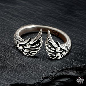 Side profile of adjustable gothic angel wing ring in 925 sterling silver displaying three-dimensional feather details. Wings curve gracefully around silver band, showing depth and shadow play. Perfect for dark academia, fallen angel style, gothic jewelry collection. Handcrafted premium silver construction.