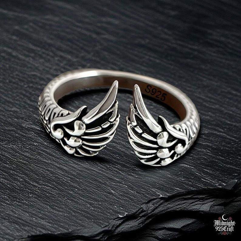 Side profile of adjustable gothic angel wing ring in 925 sterling silver displaying three-dimensional feather details. Wings curve gracefully around silver band, showing depth and shadow play. Perfect for dark academia, fallen angel style, gothic jewelry collection. Handcrafted premium silver construction.