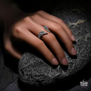 Artistic black and white photography of sterling silver gothic angel wing ring highlighting contrast and detail. Adjustable band design with dual angel wings, each feather meticulously crafted. Suitable for goth subculture, alternative fashion, dark aesthetic jewelry collection.