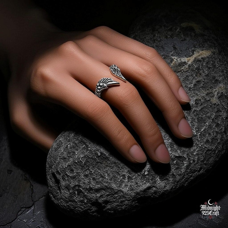 Artistic black and white photography of sterling silver gothic angel wing ring highlighting contrast and detail. Adjustable band design with dual angel wings, each feather meticulously crafted. Suitable for goth subculture, alternative fashion, dark aesthetic jewelry collection.