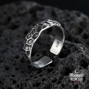 May include: A silver ring with a textured, honeycomb-like pattern. The ring is open at the bottom and stamped with "925" and "525". The ring is set against a dark, textured background. The Midnight 925 Craft logo is visible.