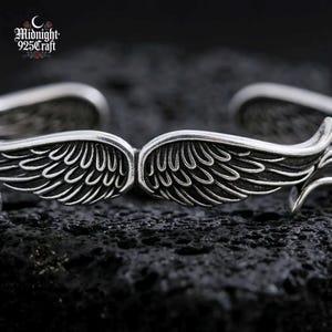 Top-down view of the Angel Wings 925 sterling silver bracelet showing paired wing motifs meeting at the center of the cuff. The intricate feather engraving detail reflects light beautifully, showcasing its artisanal quality. Suitable as a memorial bracelet, guardian angel gift, or couple matching jewelry.