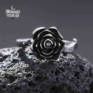 May include: A silver-toned ring featuring a detailed rose design. The rose is the focal point, with intricate petal detailing. The ring band has a textured design. The brand name "Midnight 925 Craft" is visible in the upper left corner.