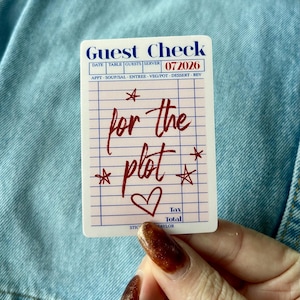 May include: A white sticker with a "Guest Check" header and the date "072026". The sticker has a grid pattern with the words "for the plot" in red script, along with star and heart illustrations.