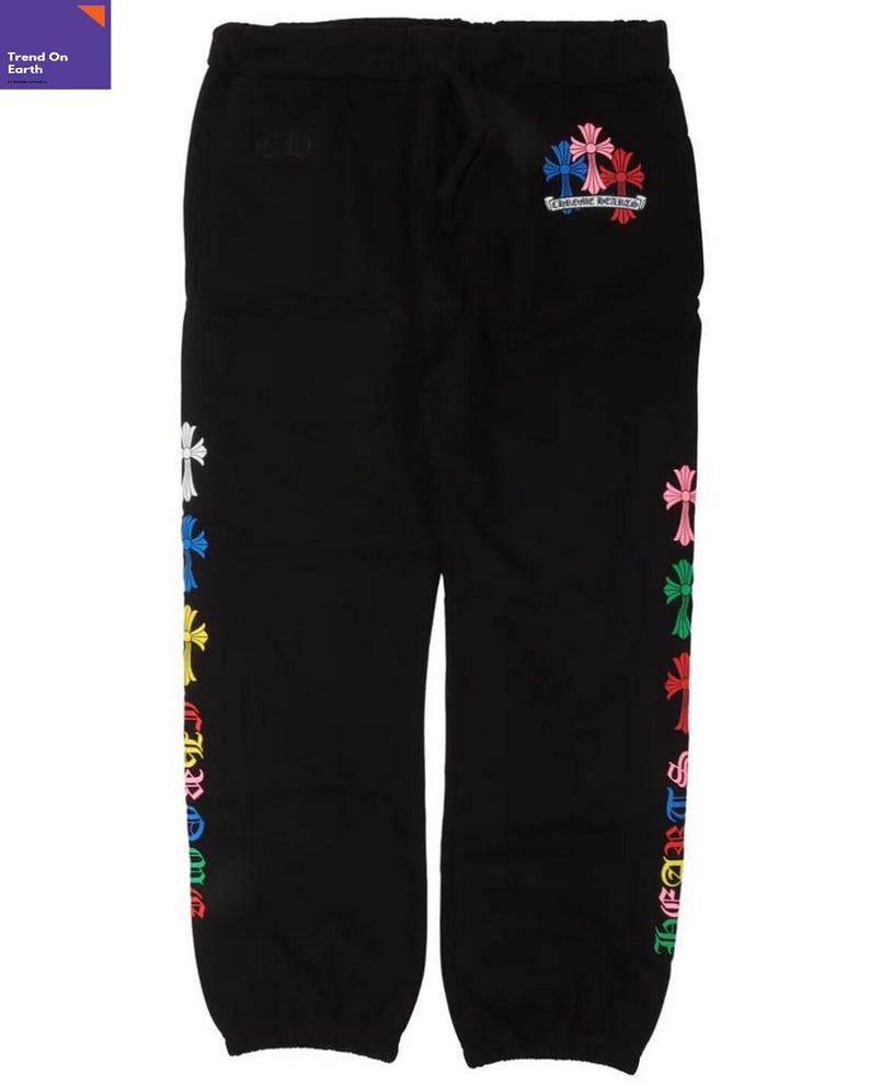 Op de afbeelding: Zwarte joggingbroek met een trekkoord in de taille en kleurrijke kruisontwerpen geborduurd op de zijkant en achterkant. De kruisen zijn in verschillende kleuren, waaronder wit, blauw, roze en groen. De tekst "Chrome Hearts" is ook zichtbaar.