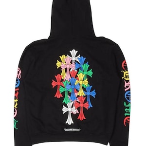 Op de afbeelding: Zwarte hoodie met een kleurrijk kruisontwerp op de rug en mouwen. Het ontwerp bevat meerdere kruisen in verschillende kleuren, waaronder rood, geel, blauw en wit. De mouwen hebben tekst in een regenboogkleurenschema. De hoodie heeft een capuchon.