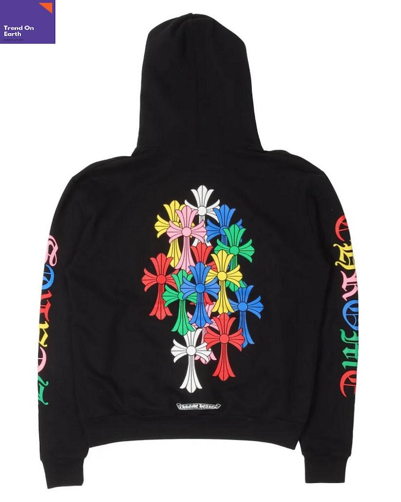 Op de afbeelding: Zwarte hoodie met een kleurrijk kruisontwerp op de rug en mouwen. Het ontwerp bevat meerdere kruisen in verschillende kleuren, waaronder rood, geel, blauw en wit. De mouwen hebben tekst in een regenboogkleurenschema. De hoodie heeft een capuchon.